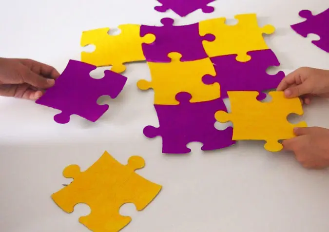 Drei Hände puzzeln großes gelb und lila farbenes Puzzle 