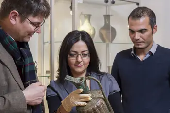Der Inhaber der Professur für Islamische Kunstgeschichte und Archäologie (li.) Lorenz Korn steht mit zwei Studierenden vor einer Vitrine mit Vasen im Bamberger Universitätsmuseum für Islamische Kunst. Alle drei schauen auf eine Vase, die die Studentin in den Händen hält.  
