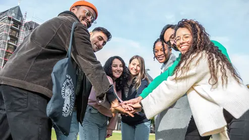 mehrere Studierende legen je eine Hand in die Mitte und stehen im Kreis