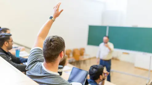 Students in a lecture hall at the university Studierende melden sich im Hörsaal während einer Veranstaltung