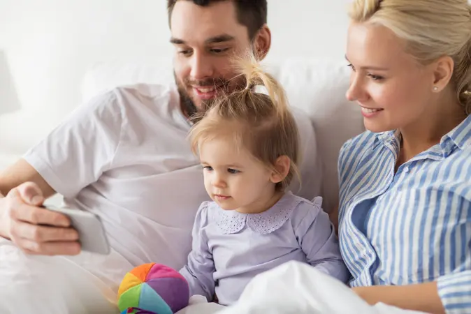 happy family with smartphone in bed at home