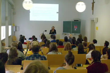 Impressions of Prof. Dr. Marcia Pally giving her talk and attendees listening to her.