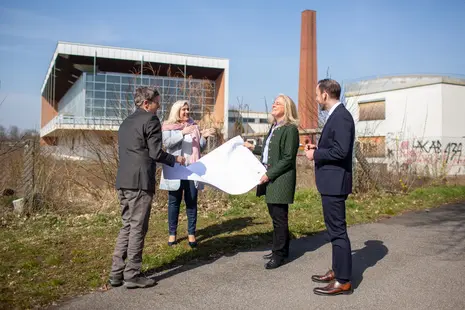 Bauamtsleiter Jürgen König zeigt der Staatsministerin Melanie Huml, der Kanzlerin der Universität Dagmar Steuer-Flieser sowie dem Universitätspräsidenten Kai Fischbach (v.l.n.r.) die Baupläne zum alten Hallenbad. 