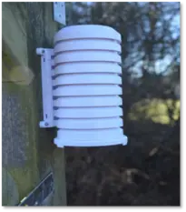 Das Außenmodul einer Netatmo Smart Weather Station, an eine Wand montiert. Im Hintergrund ist ein Baum zu sehen.