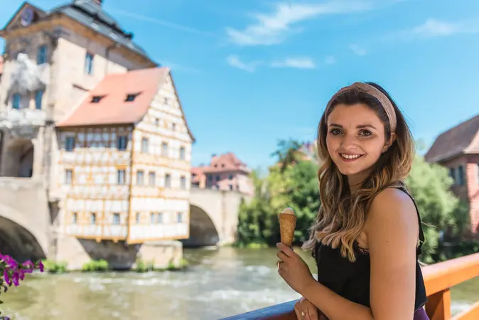 Eine Studentin isst Eis am Alten Rathaus – das Wahrzeichen von Bamberg ist in den Fluss Regnitz gebaut.