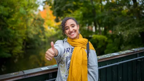 Student in Bamberg Studentin zeigt einen Daumen nach oben und steht am Alten Kanal in Bamberg