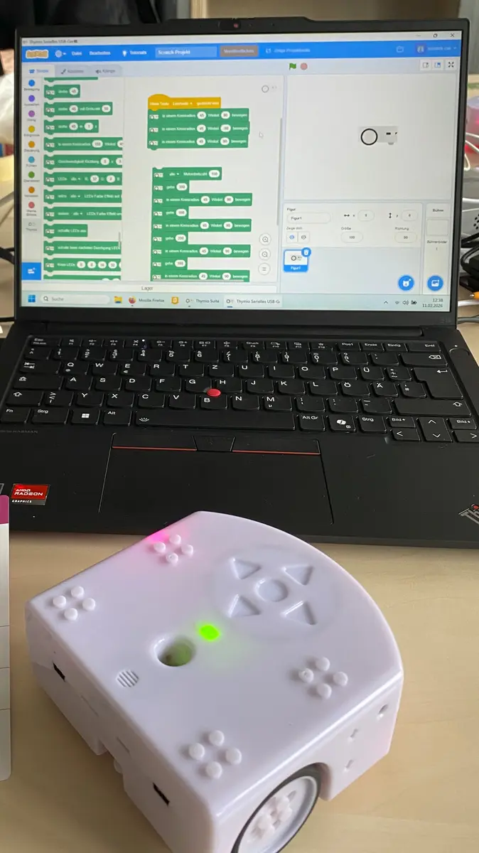 Laptop mit Scratch-Programmierung auf dem Bildschirm, davor ein Thymio-Roboter