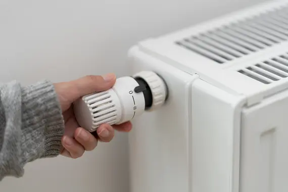 Eine Hand dreht am Temperaturregler eines Heizkörpers.