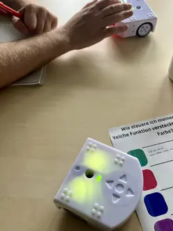 eine Hand, die einen Thymio-Roboter bedient, während ein anderer über das Arbeitsblatt fährt