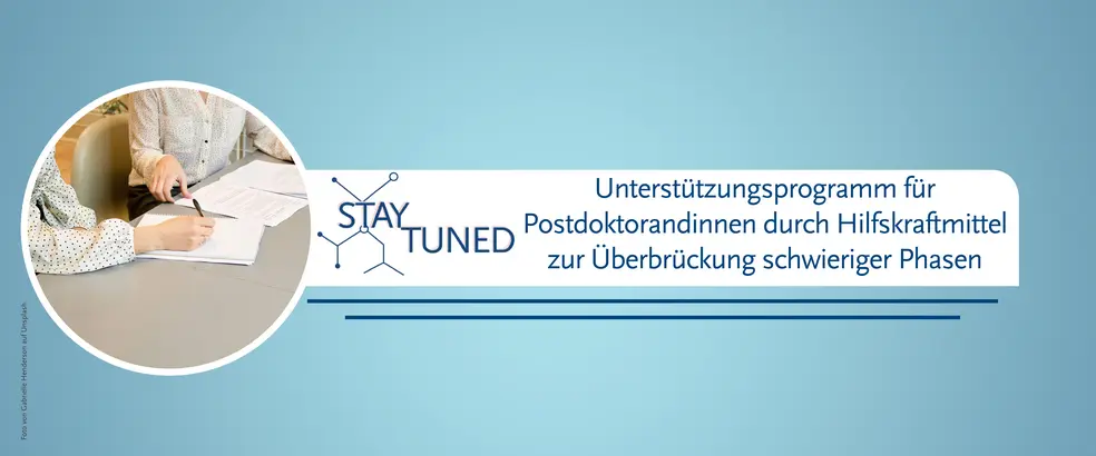Zu sehen ist ein Banner mit blauem Hintergrund für die Seite von 'StayTuned - Unterstützungsprogramm für Postdoktorandinnen durch Hilfskraftmittel zur Überbrückung schwieriger Phasen'. In einem kreisrunden Bild sind zwei sitzende Frauen zu sehen, wobei eine von ihnen einen Kuli hält, während auf dem Tisch Papiere liegen.