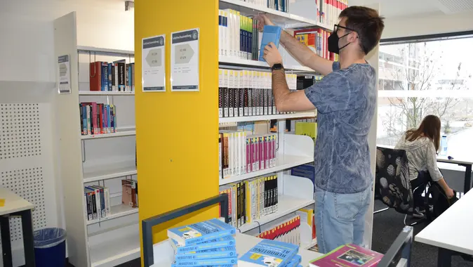 Ein Mitarbeiter der Universitätsbibliothek räumt das Buch „Rebooting AI“ in ein Regal.