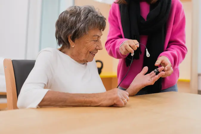 Ältere Dame hat Sensoren an den Fingern, jüngere Dame verkabelt diese