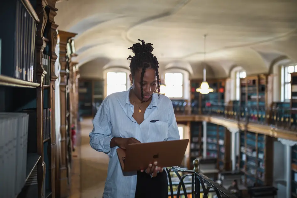 Woman standing in library staring intensely at laptop