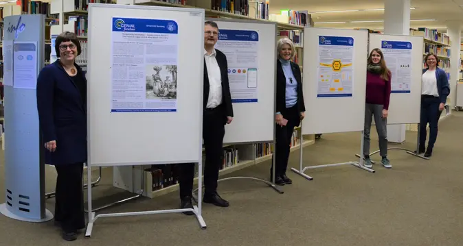 Das Team des Projekts „GENIAL forschen“ sowie Bibliotheksdirektor Fabian Franke stehen neben Plakaten bei der Eröffnung der Posterausstellung.