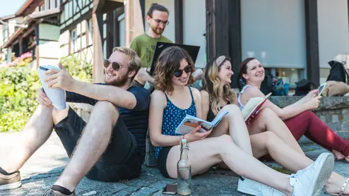 Studierende sitzen vor der TB5 am Wasser und lernen