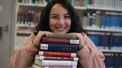 Studentin mit einem Stapel Bücher in der Uni-Bibliothek