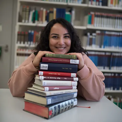 Studentin mit einem Stapel Bücher in der Uni-Bibliothek