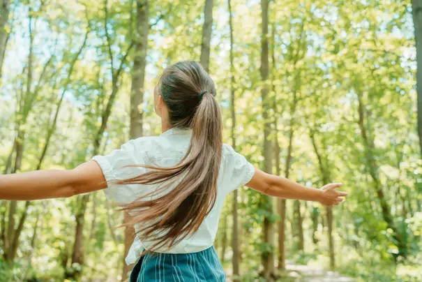 Happy woman in forest with open arms from behind breathing clean air. Environment, no pollution healthy natural living lifestyle. Free spirit in the woods