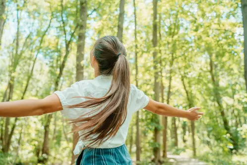 Happy woman in forest with open arms from behind breathing clean air. Environment, no pollution healthy natural living lifestyle. Free spirit in the woods