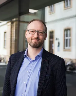 Portrait Frank Schiemann, lächelnd vor Uni-Gebäude