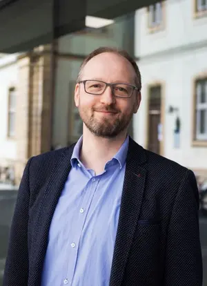 Portrait Frank Schiemann, lächelnd vor Uni-Gebäude