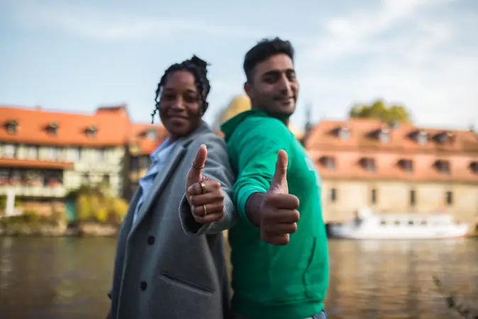Zwei Studierende stehen vor der Kulisse Bambergs und zeigen die Daumen nach oben.
