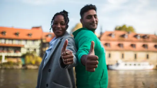 Zwei Studierende stehen vor der Kulisse Bambergs und zeigen die Daumen nach oben.