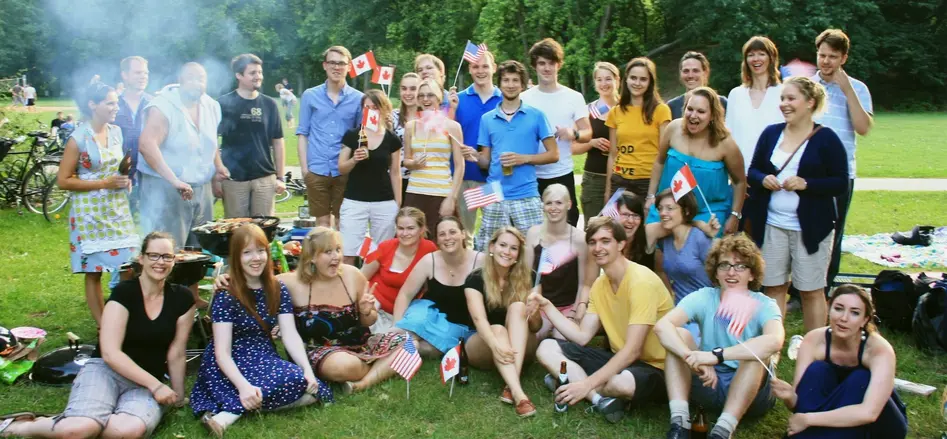 [Translate to 1 - english:] Group photo of participants of “Bamberg Buddies” having a good time at a barbecue party in the Hain Park, waving US and Canadian flags.