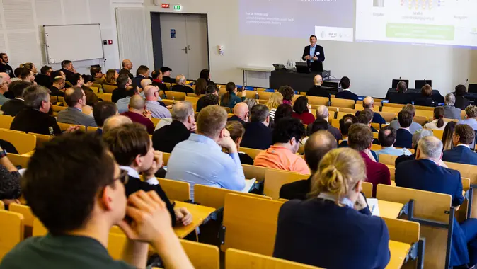 Viele Personen hören einem Professor in einem Hörsaal zu.