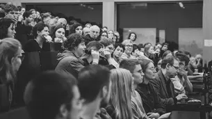 A black-and-white photo of the audience taken in profile. A female student is in the process of asking a question.