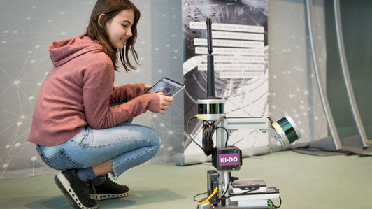Ein Mädchen hält ein Tablet in der Hand und steuert einen Roboter.