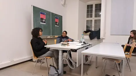 Das Foto zeigt die afrodeutsche Autorin Patricia Eckermann, links, und die afro-amerikanische Wissenschaftlerin Professor Tiffany N. Florvil, rechts. Sie sitzen nebeneinander an der Stirnseite eines Seminarraums und unterhalten sich.
