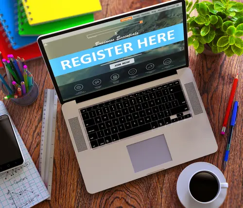 Es ist ein Laptop zu sehen. Der Bildschirm zeigt die Worte "Register Here".