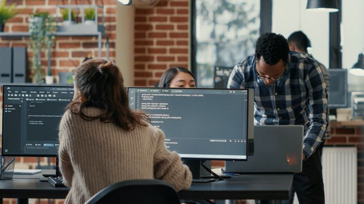 Drei Menschen arbeiten an Computern und Laptop.