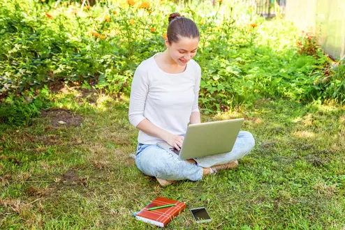 Young woman sitting on green grass lawn in city park working on laptop pc computer. Freelance business concept