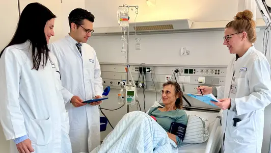 Patientin und Ärztinnen und Arzt in einem Patientenzimmer am Krankenbett.