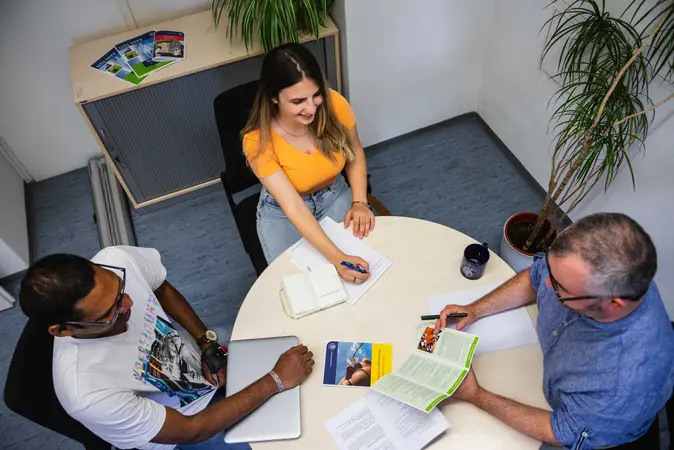 Zwei Personen bekomme in einem Büro Informationen von einem Studienberater.