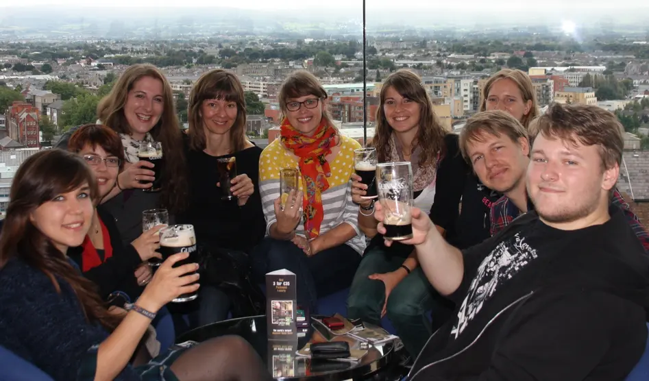 Group photo of the seminar members enjoying pints of Guinness at the Guinness storehouse with Dublin in the background.