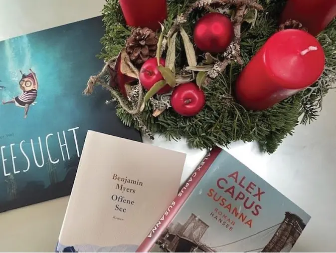 Neben einem Adventskranz liegen drei Bücher.