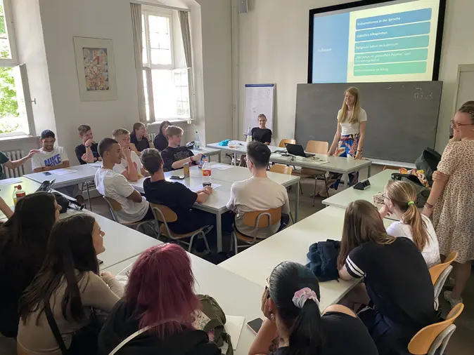 Schüler:innen in einem Seminarraum, die der Dozentin zuhören.