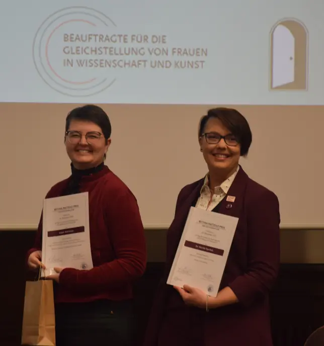 Das Foto zeigt zwei weiße Frauen die Urkunden halten.