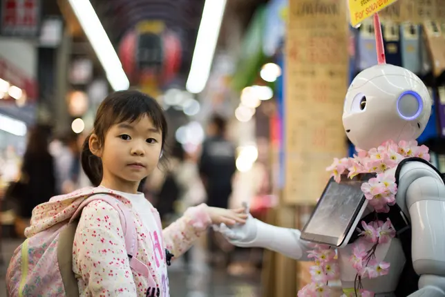 Ein kleines Mädchen gibt einem Roboter die Hand.