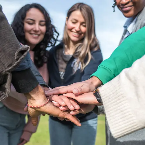 Studierende legen gemeinsam je eine Hand in der Mitte und stehen im Kreis