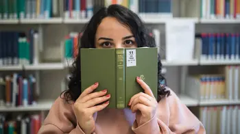 In der Bibliothek Studentin schaut über den Rand eines Buches in der Bibliothek