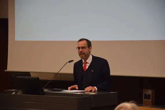Der Präsident der Universität, Prof. Dr. Kai Fischbach steht an einem Pult mit einem Mikrofon vor ihm