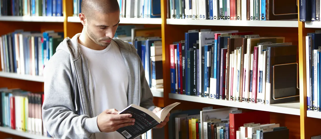 inside, daylight, people, european, scandinavian, danish, college student, student, study, university, college, education, school, learn, library, book, shelf, assortment, man, 19, caucasian, 19, serious look, concentration, hooded sweatshirt, bald, caucasian, 20, man