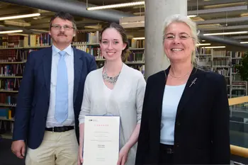 Die Auszubildende der Universitätsbibliothek Leoni Schmalz, Beste ihres Jahrgangs, mit ihrer Urkunde vor einem Bücherregal in der Teilbibliothek 4. Links neben ihr Bibliotheksdirektor Dr. Fabian Franke, rechts neben ihr Kanzlerin Dr. Dagmar Steuer-Flieser.