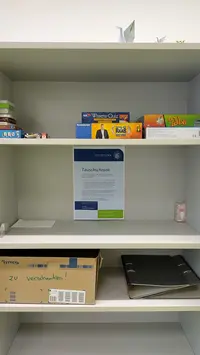 Tauschschrank im MG2 Das Bild zeigt ein Regal mit einzelnen Gegenständen, die zu verschenken sind, zum Beispiel Spiele, Ordner und Kleinigkeiten.