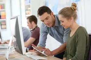 Schülerin arbeitet mit Hilfe eines Lehrers an Computer und Tablet