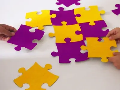 Drei Hände puzzeln großes gelb und lila farbenes Puzzle 